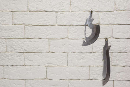 There are two kinds of knife blades hanging on the light brick wall on the right side.