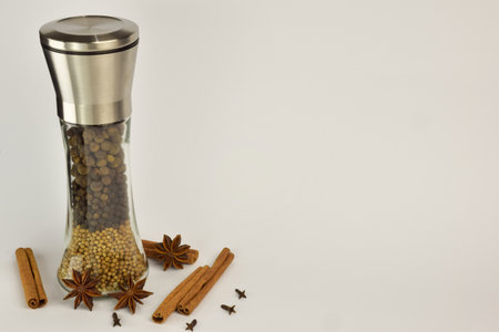 Pepper mill with different types of peppers in layers, as well as stars of anise and cinnamon on a white background. On the right is a place for an inscriptionの写真素材