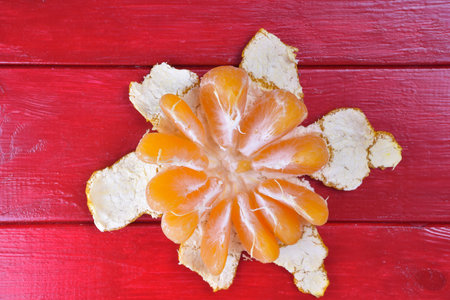 A half-peeled tangerine lies on a red wooden background in the center of the frameの写真素材