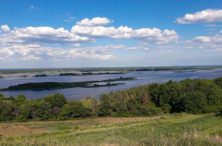 Below, under the hill, there is a wide river against the background of light clouds and a bright...