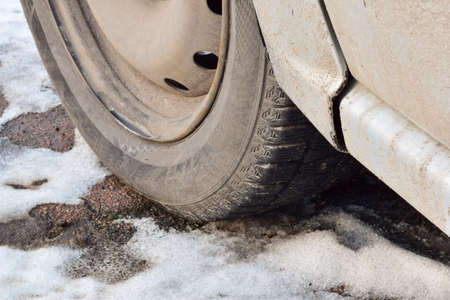 On wet snowy asphalt close-up dirty wheel of a passenger car
