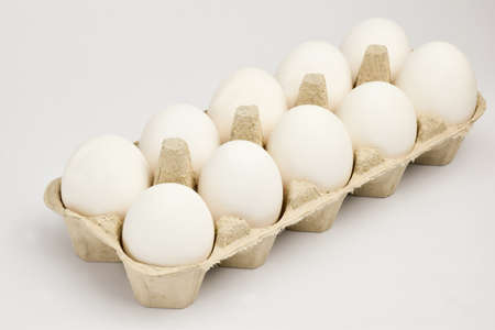Ten chicken eggs lie in two rows in a cardboard tray. The tray lies obliquely