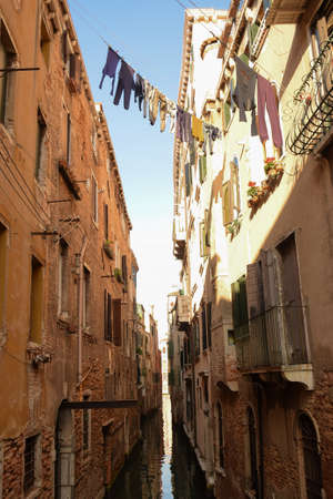 A canal in Venice, Italy, between old buildings with washed residents' clothes hanging between them, rows of windows and balconiesの写真素材