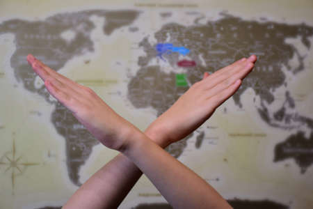 Two crossed human hands in a prohibition sign in front of a world map with a highly blurred backgroundの写真素材