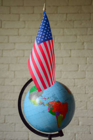 The USA flag is set against a background of a heavily blurred world globe and brick wall. Blurred...