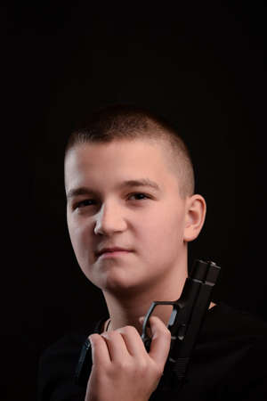 Young guy with a gun with a short haircut on a very dark background. Looks straight into the cameraの写真素材