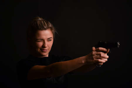 A young girl takes aim from a pistol she holds with two hands. The face is in sharp focus, and the weapon is out of focus. Photographed against a very dark backgroundの写真素材