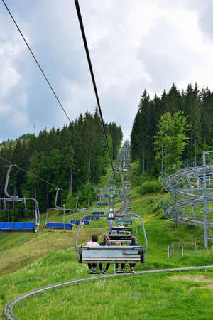 A lift with many benches takes people up the mountain covered with trees. Photo taken in summer,...