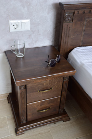 Sunglasses and an empty glass lie on a decorative brown wooden nightstand near the bed. Wall mounted electrical outlet and light switchの写真素材