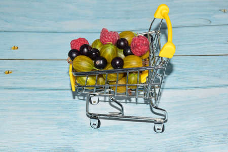 Raspberries, gooseberries and currants are stacked in a small toy shopping cart. Photographed close-upの写真素材
