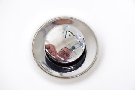 Reflection of a man in glasses who brushes his teeth in the bath on a shiny cork stopping the drain of water. Close-upの写真素材