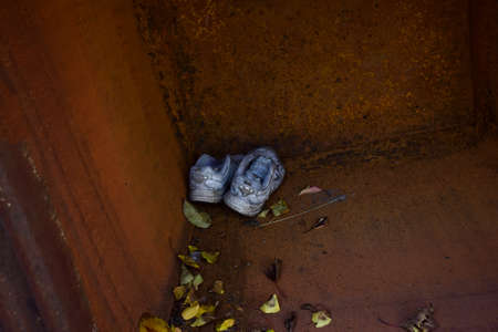 In the corner of a rusty tank with brown walls, lie a pair of worn out old sneakers near yellow leavesの写真素材