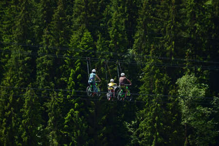 Parents and a child of unrecognizable appearance ride special bicycles, sliding along the ropes on an attraction high above the groundの写真素材