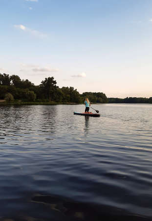 Athletic girl swims on a paddle board for swimming supa on her knees and helps herself with a paddle