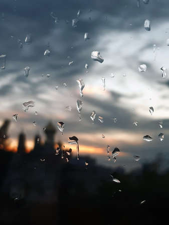 There are many drops of water on the glass. Blurred buildings and sky behind glassの写真素材