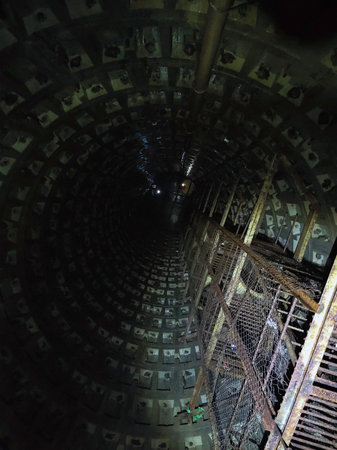A vertical shaft of a sewage collector with rusty stairs to the top and concrete walls. View from...
