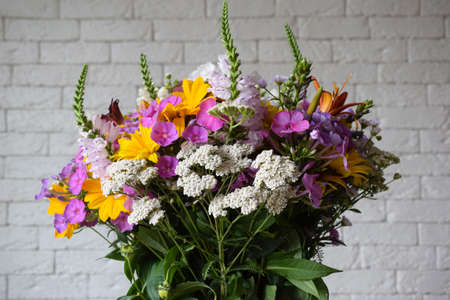 A bouquet of field various fresh flowers on a blurred brick wall backgroundの写真素材