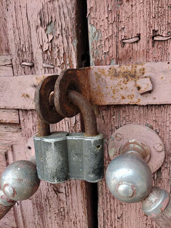 A padlock hangs on a closed door with handles of an ancient house. Shot in close-up