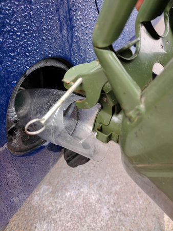 Filling fuel into the gas tank of a car from an iron can close-up. The car is wet