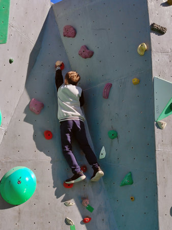 A teenage boy climbs the wall to climb the hooks. A wall on the street. View from below