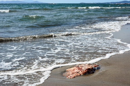 A view of a sandy sea or ocean beach and a large stone in it. Foamy waves are floating on the shoreの写真素材
