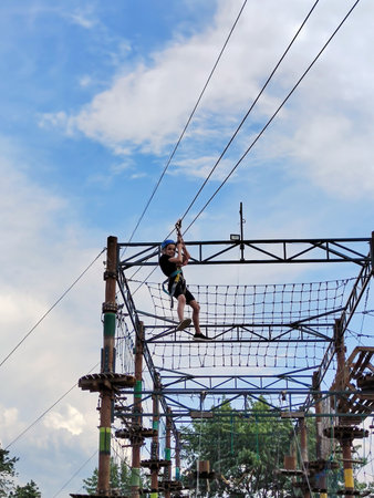 A teenage boy in a sports safety helmet and safety equipment is going down a cable car in a rope...