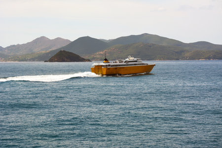 A small ferry transport ship sails to the other shore in a sea bay with small mountains or hills in the backgroundの写真素材