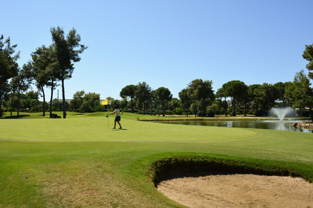 A young woman on the green of a private golf club adjusts the flag near the hole. Active summer luxury vacationの写真素材