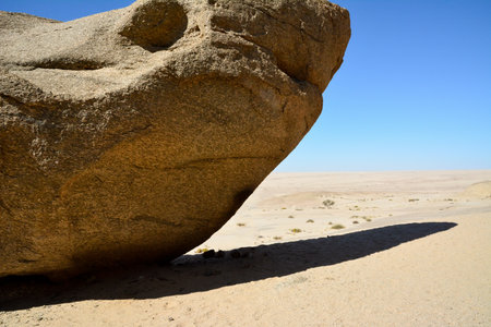 A huge rocky boulder with a shadow lies in the desert under a blue skyの写真素材
