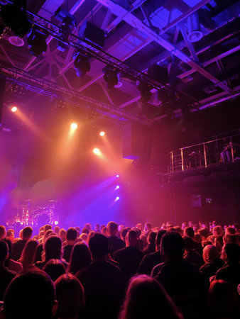 Brightly lit scene of a rock concert. There are many spectators in the hall. View from the hall