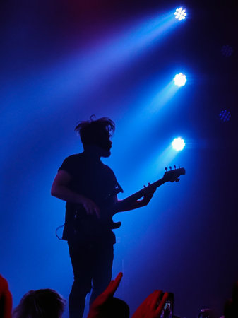 Musician guitarist playing guitar solo in blue spotlights on stage. An unidentified person and a...