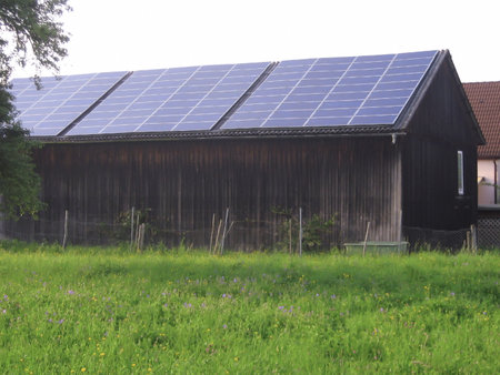 Solar panels are installed on the roof of a private barn to collect solar energy. Barn on green grass. Renewable green energy and nature conservationの写真素材