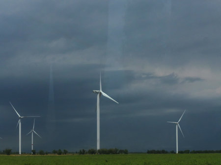 Many wind turbines are installed in the background of a wheat field against a cloudy rainy sky....