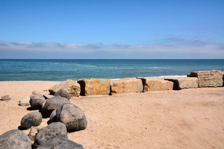 Stone boulders are laid out on the sandy sea beach to protect against storm waves. Natural tourist landscapeの写真素材