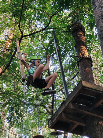 A teenage boy in a rope park in an amusement park moves on a suspended handrail. View from below on...