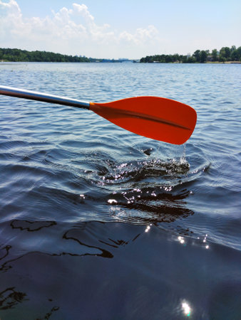 The oar of the boat is red on the background of the water of the wide river and the blue skyの写真素材