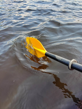 A yellow plastic oar of a boat in the water of the river scoops up the water. Summer sports and...
