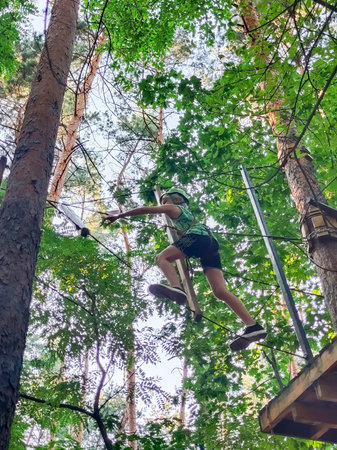 A teenage boy in an amusement park on a rope bridge crosses the rope. View from below on the...