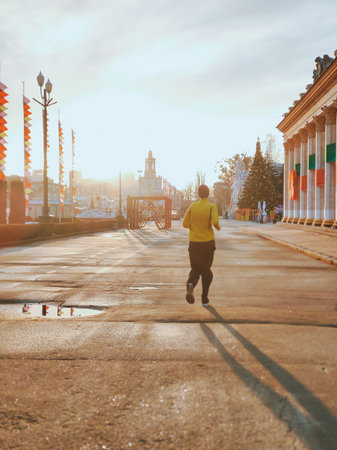A man runs at sunset with an evening jog. Rear perspective view near a large buildingの写真素材