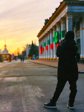 A teenage boy in a hat and jacket takes pictures of interesting historical places on a camera. Rear view in perspectiveの写真素材