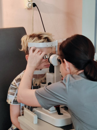 A teenage boy with dyed hair is checked by an ophthalmologist using a special device in a hospital...