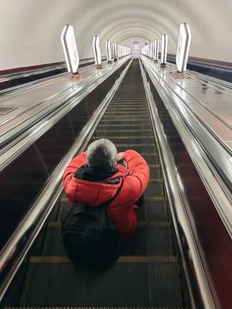 A man with a backpack sits on the steps of the escalator and goes down to the subway. Rear viewの写真素材
