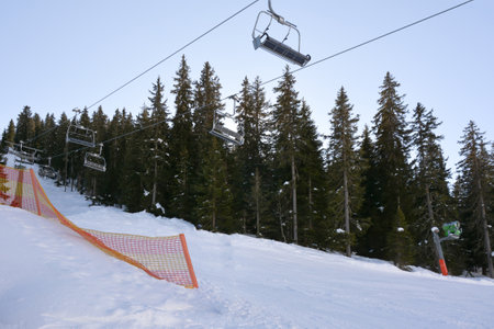 The slope of a ski slope is covered with snow. Above it, empty benches of a ski lift. Nearby a row of trees.Winter landscape and active recreationの写真素材