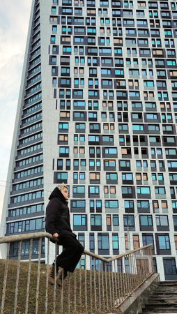 A Caucasian teenager sits on the railing of a fence against a skyscraper. A modernist-style house with many windows in perspectiveの写真素材