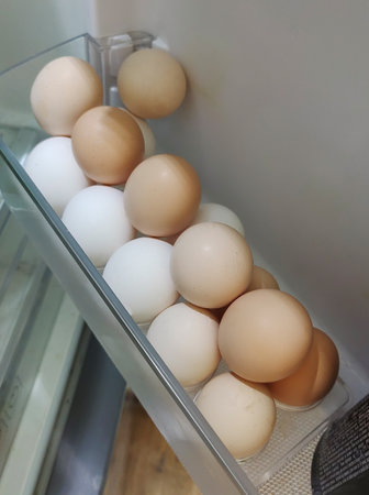 Tray of chicken eggs of different colors on a shelf in the open refrigerator door. Top view.