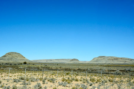 A fence in a desert landscape with small hills visible behind it under a clear blue sky. Global warming and heatの写真素材