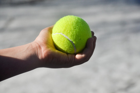 Yellow tennis ball, illuminated by the sun, lies in a child's hands.の写真素材