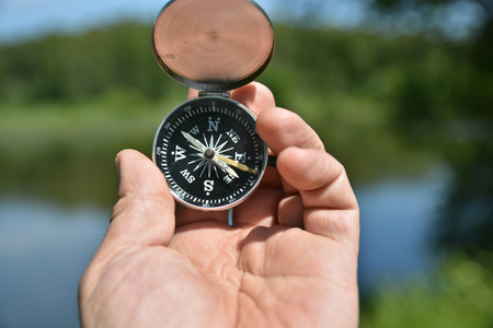 Man's hand holding compass on the contrary refocusing summer landscape.