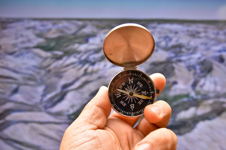 Compass in hand on background of the relief. Man's hand holds a magnetic compass.の写真素材