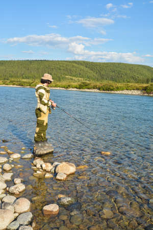 Fisherman on the river. A young man fishes with a spinning rod on the northern pebble river.